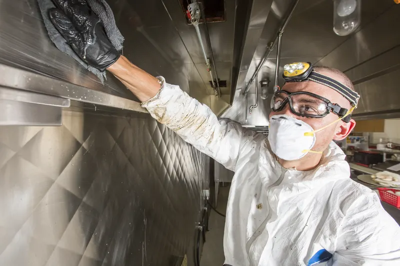 Technician reaching into the chamber behind a removed filter of a stainless steel commercial kitchen exhaust hood