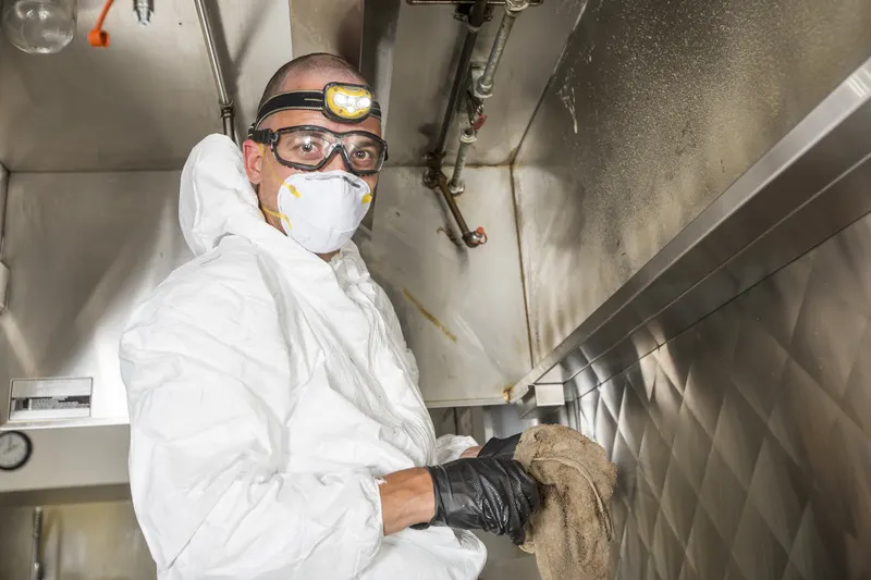Worker scrubbing the empty filter channel along the front lip of a commercial exhaust hood
